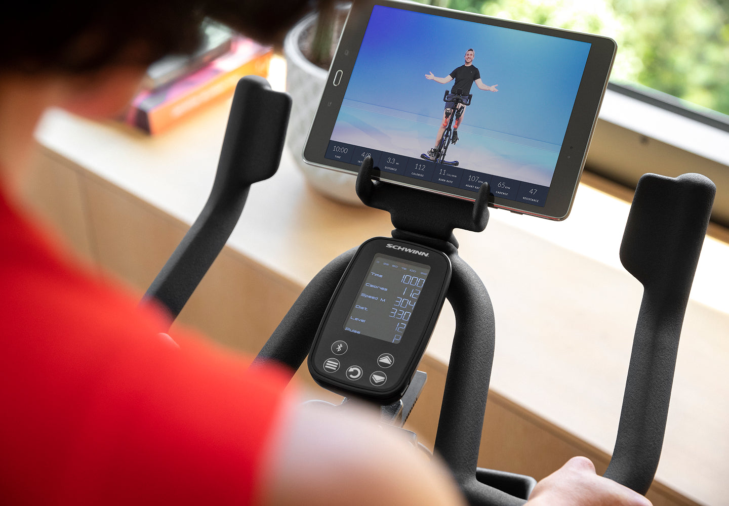 A rider in a red top looks at a tablet on the Schwinn IC4 handlebar, with the console below it